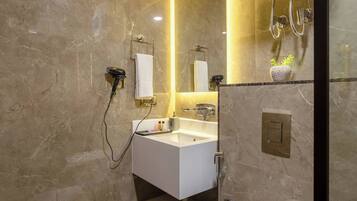 A modern bathroom with a marble wall, a white sink, a toilet, and a shower area.