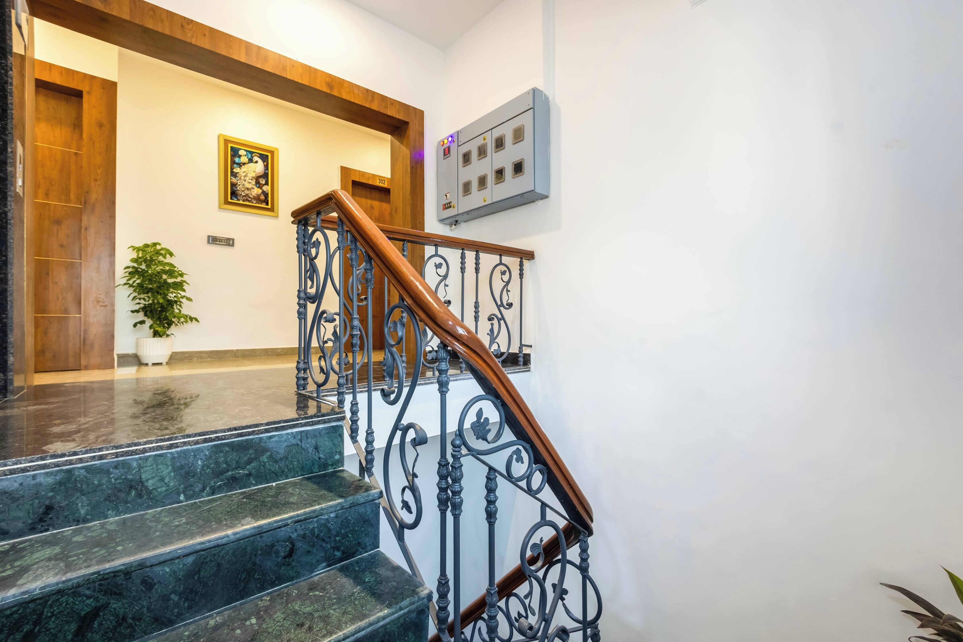 Una escalera con barandilla de madera y barandales de metal negro, que conduce a un rellano con una puerta de madera y un cuadro enmarcado en la pared.