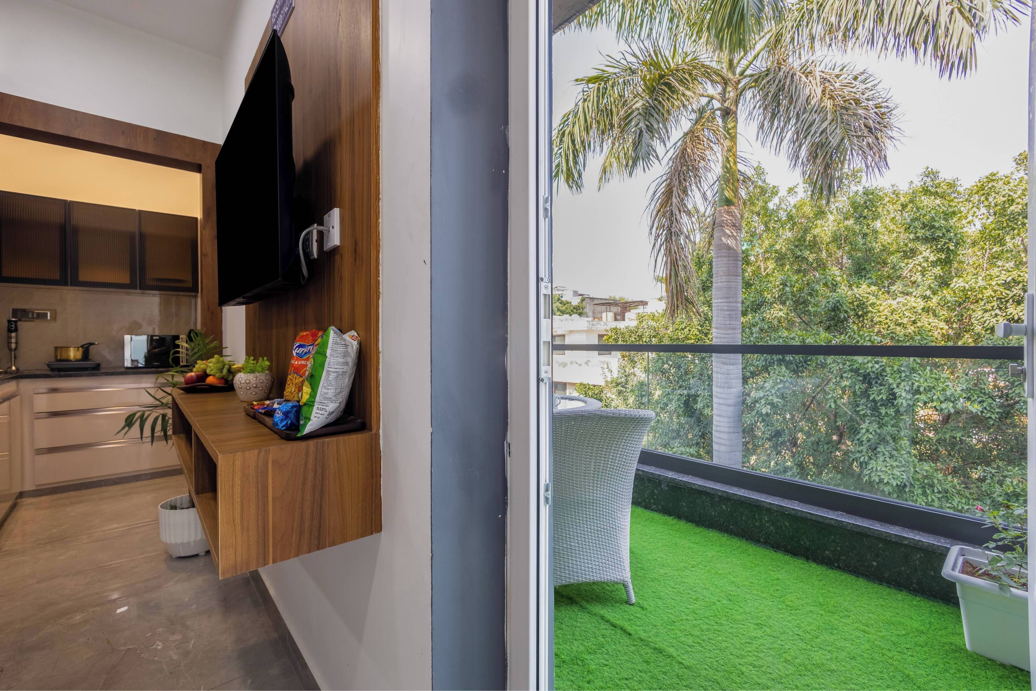 A modern kitchen with a flat-screen TV, wooden cabinets, and a dining area with a wicker chair.