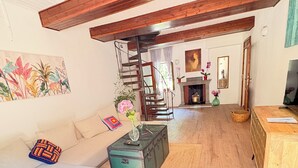 Ein geräumiges Wohnzimmer mit hoher Decke, einer Treppe, einem Kamin und einem Fernseher.