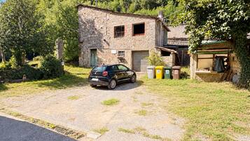Ein rustikales Steinhaus mit einem geparkten Auto davor, umgeben von viel Grün und Bäumen.