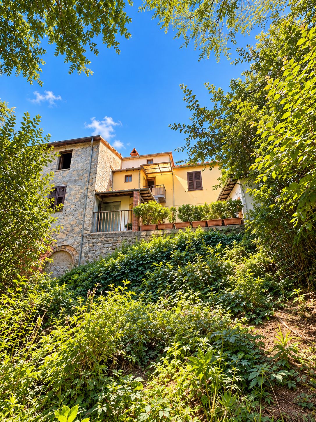 A stone building with a balcony, surrounded by lush greenery.