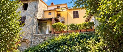 A stone building with a balcony, surrounded by lush greenery.