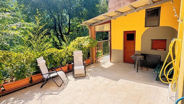Eine Terrasse mit zwei Lounge-Stühlen, einem Tisch und einem gelben Gebäude mit Tür und Fenster.