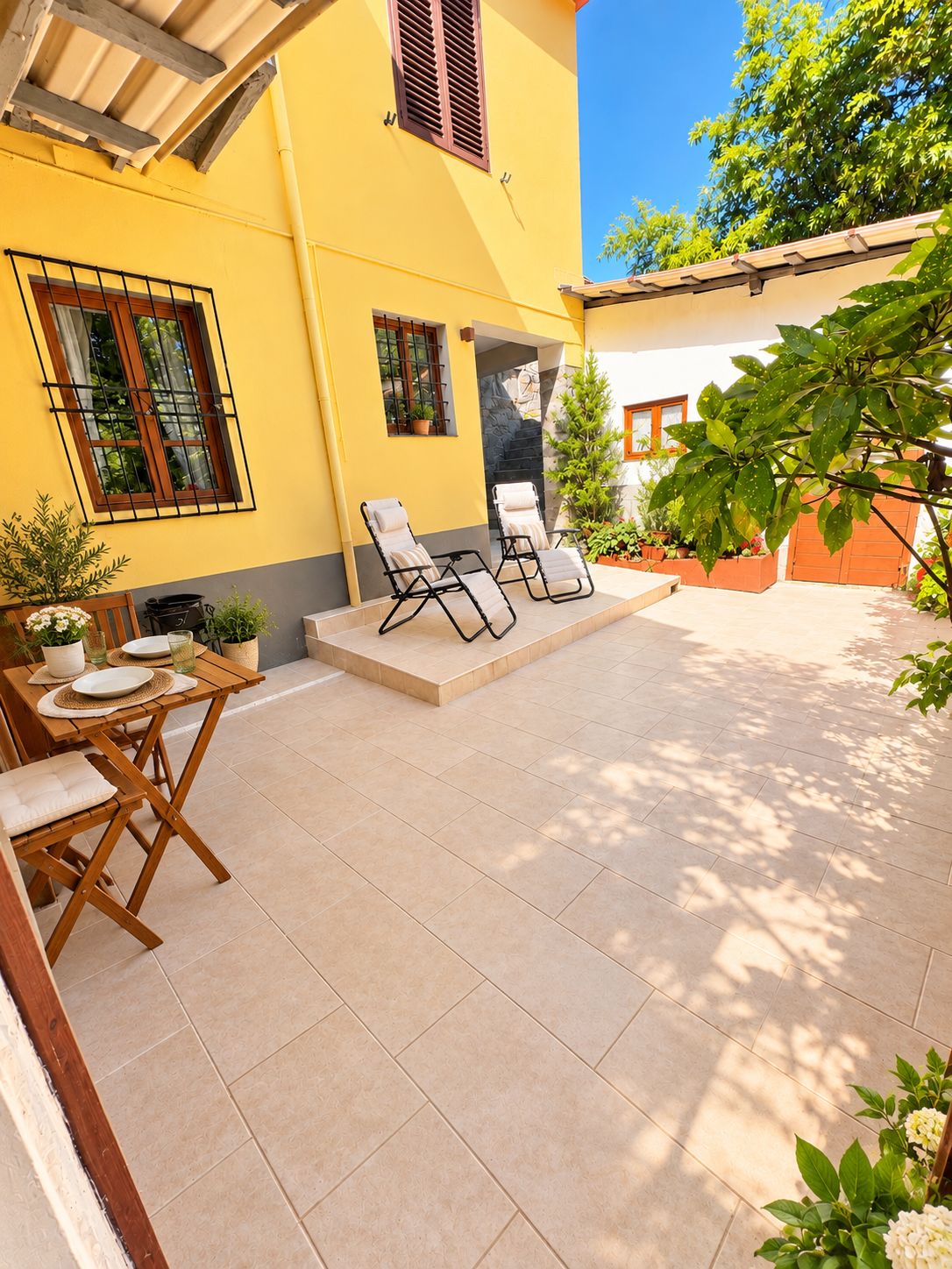 A yellow building with a patio area featuring outdoor seating and potted plants.