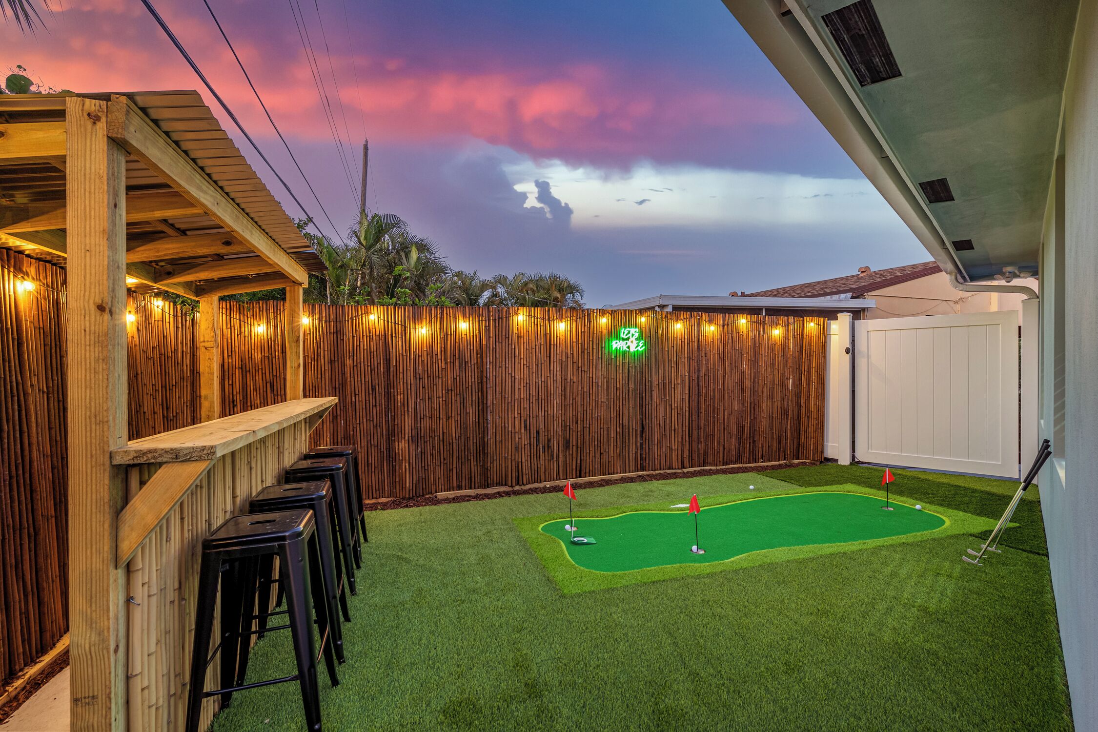 A backyard with a mini-golf setup, a wooden deck, and a bamboo fence.