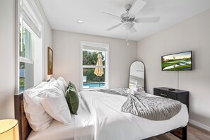 Une chambre à coucher avec un lit, un ventilateur de plafond, une télévision et une fenêtre avec un parapluie.