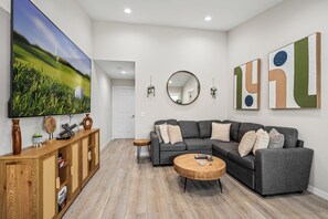 Un salon moderne avec un canapé d’angle, une table basse, un téléviseur et des œuvres d’art décoratives au mur.