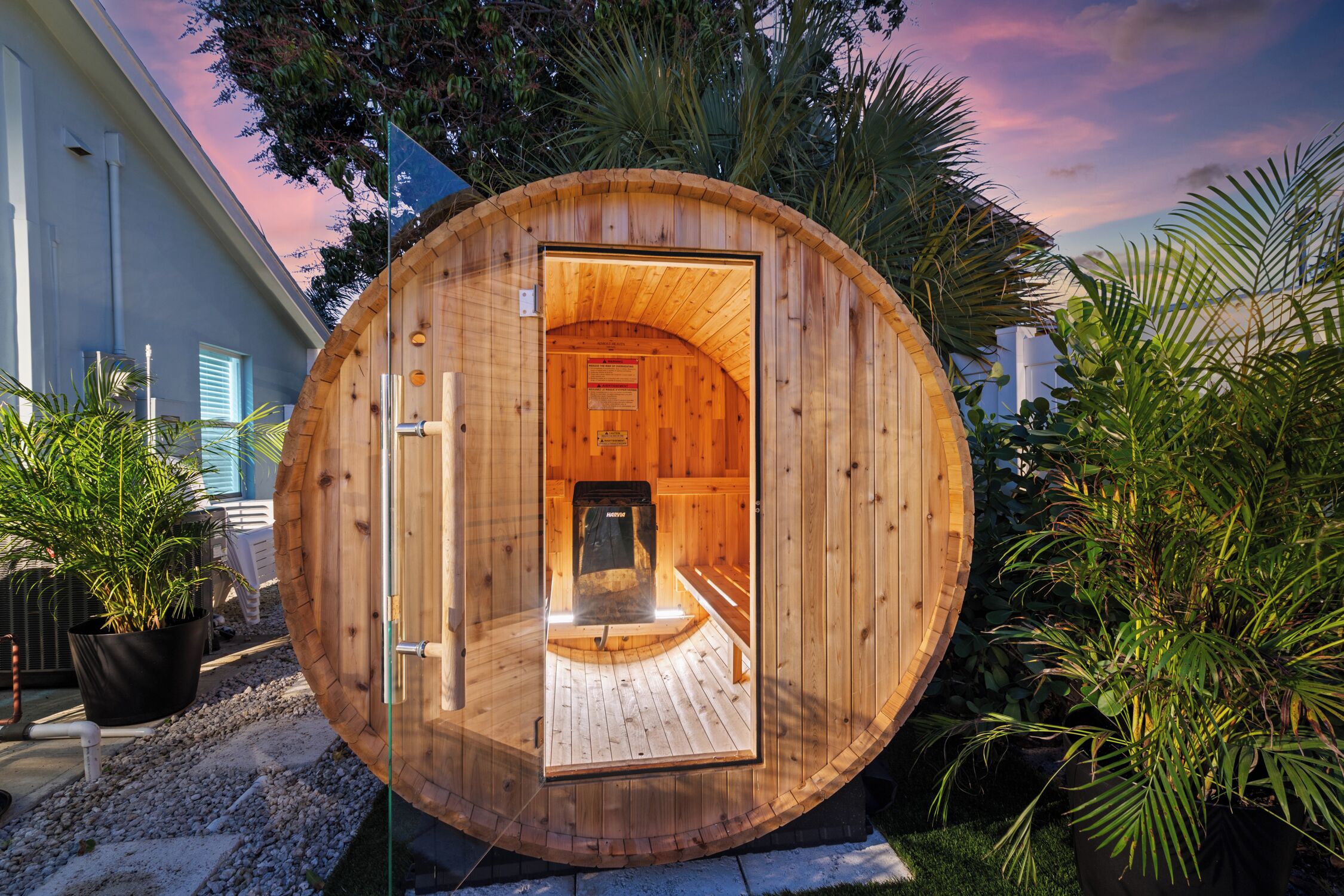 A wooden sauna structure with a glass door, surrounded by greenery.