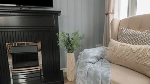 A living room with a black fireplace, a beige sofa with patterned cushions, and a potted plant. - Sea Glass Lodge (Saltburn-by-the-Sea)