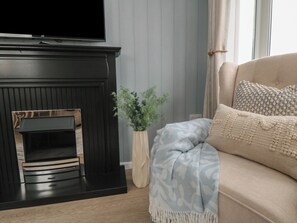 Ein Wohnzimmer mit einem schwarzen Kamin, einem beigen Sofa mit gemusterten Kissen und einer Topfpflanze.