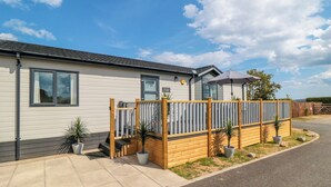 A single-story mobile home with a fenced patio area, potted plants, and a clear sky. - Sea Glass Lodge (Saltburn-by-the-Sea)