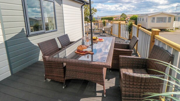 An outdoor patio with wicker furniture, a table, and a large umbrella. - Sea Glass Lodge (Saltburn-by-the-Sea)