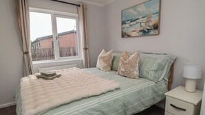 A bedroom with a bed, pillows, a bedside table with a lamp, and a painting on the wall. - Sea Glass Lodge (Saltburn-by-the-Sea)