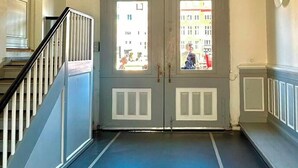 A hallway with a blue floor, a staircase with white railings, and a door with windows. - Unique panoramic view of Nyhavn from the 3rd floor (København)