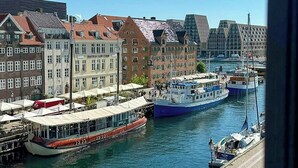 A waterfront view with a row of buildings, a dock with boats, and a pedestrian walkway. - Unique panoramic view of Nyhavn from the 3rd floor (København)