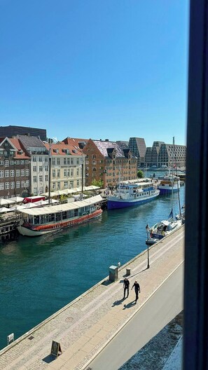 Blick auf das Wasser mit einer Reihe von Gebäuden, einem Steg mit Booten und einem Fußgängerdamm.