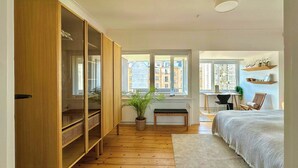 A bedroom with a large wardrobe, a bed, a desk, and a view of buildings through the window. - Unique panoramic view of Nyhavn from the 3rd floor (København)