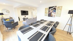 A modern living room with a large table, sofas, and a flat-screen TV. - The Kelburn - 4 bedroom house - Kilmarnock (Riccarton)