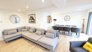 A modern living room with a sectional sofa, a dining area with chairs, a giraffe decoration, and a clock on the wall. - Kelburn, Kilmarnock - 4 bed house (Riccarton)