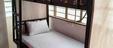 A bunk bed with a mattress and pillows, a window with a view, and a wooden door.