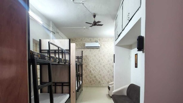 A narrow hallway with bunk beds on one side and a sofa on the other. There is a ceiling fan and an air conditioning unit visible. - Home away from home (Pune)