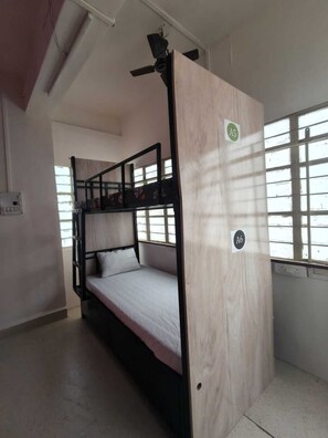 Habitación con literas, ventilador de techo, ventana con barrotes y un cartel que indica el número de habitación A5.