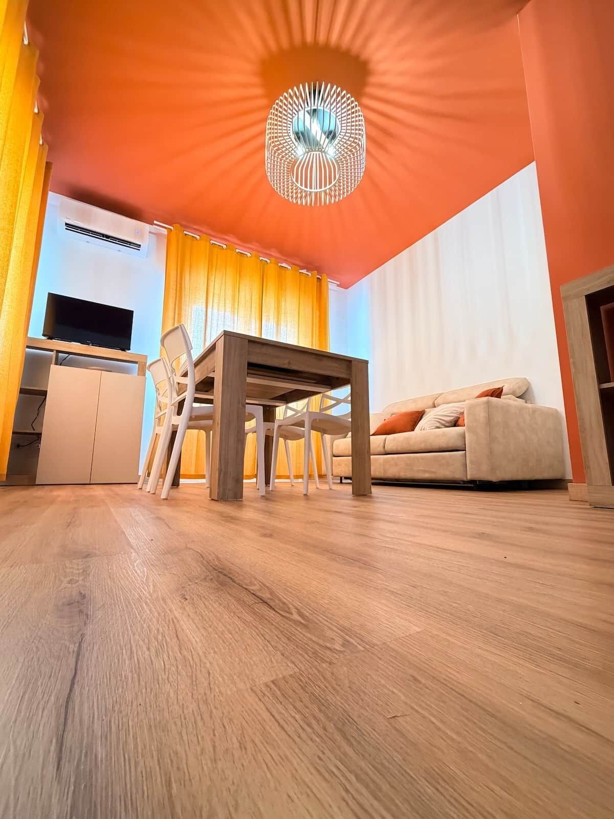 A modern living room with a wooden floor, a dining table, a sofa, and a TV.