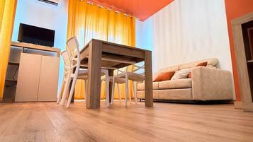 A modern living room with a wooden floor, a dining table, a sofa, and a TV.