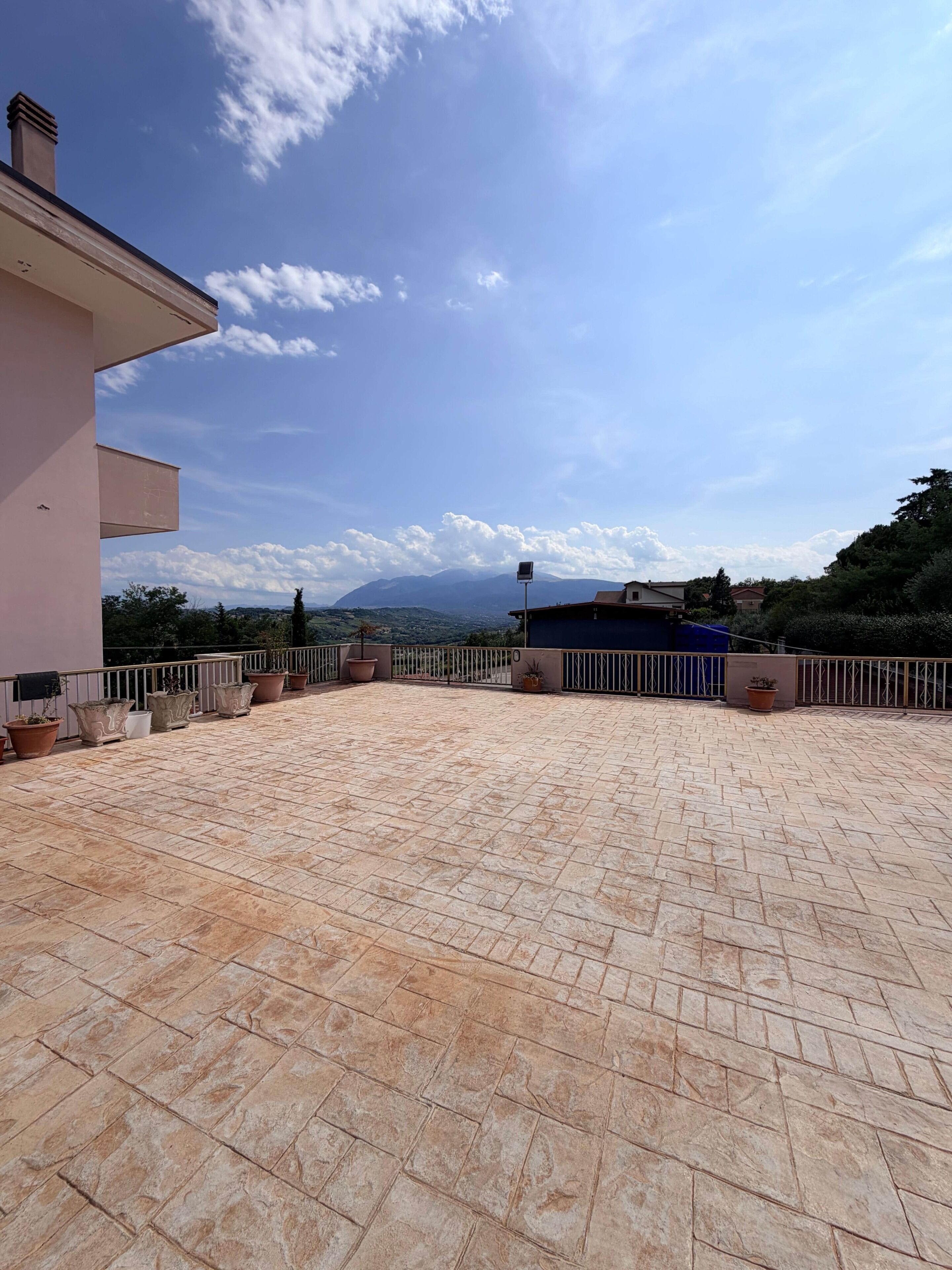 A rooftop terrace with potted plants, a clear sky, and distant mountains.
