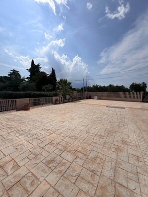 An outdoor patio area with a paved floor, surrounded by a low fence, and trees in the background.
