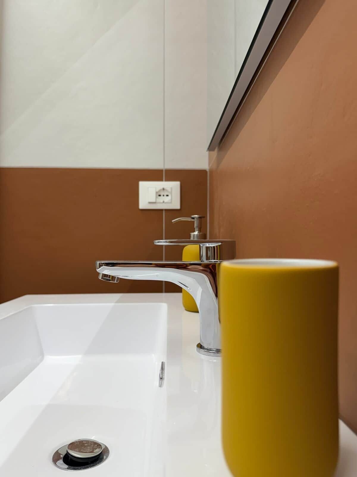 Une salle de bain avec un lavabo blanc, un robinet chromé et un vase jaune.