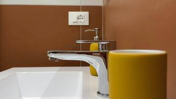 Une salle de bain avec un lavabo blanc, un robinet chromé et un vase jaune.