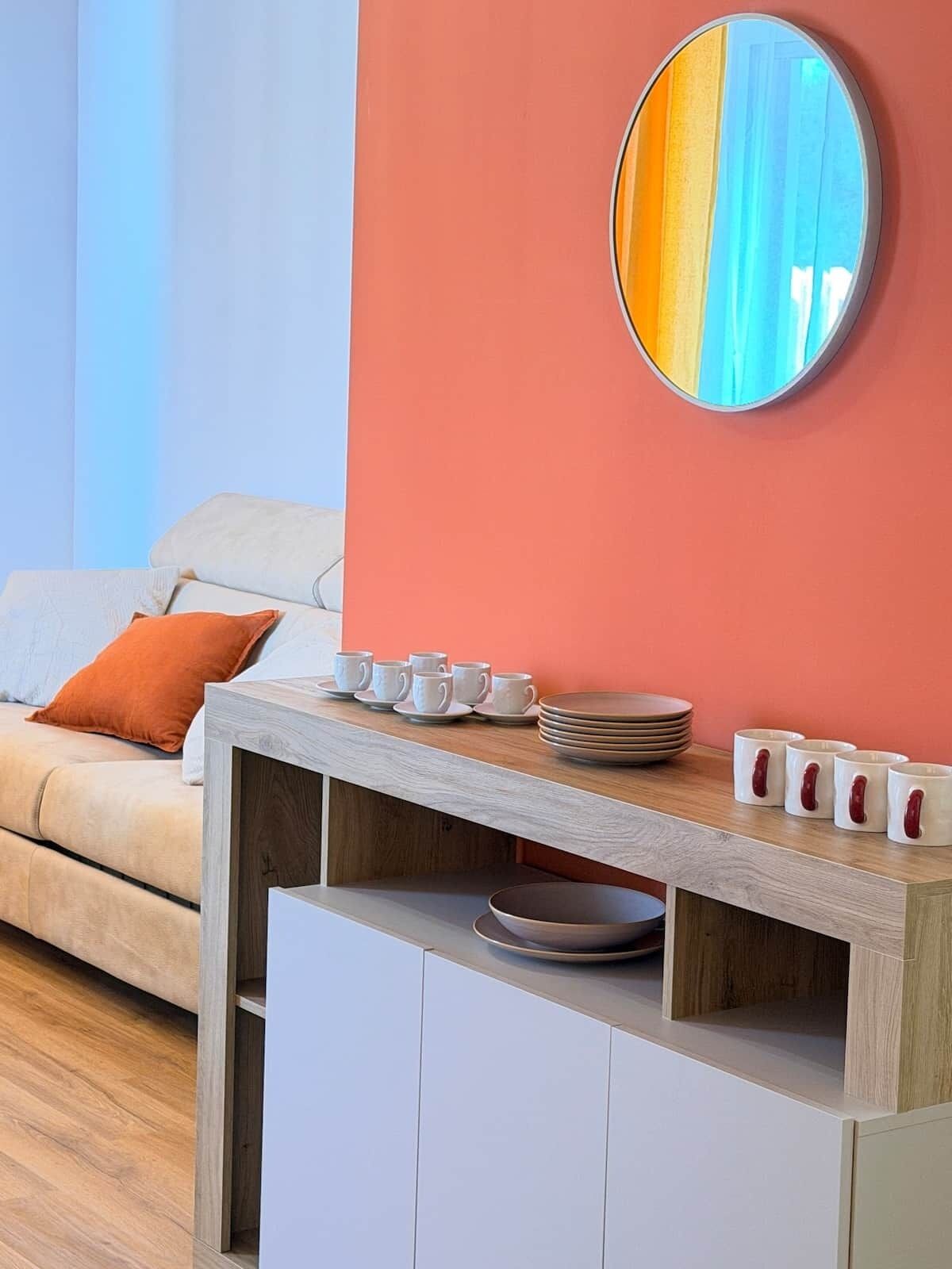Un salon moderne avec un canapé, une table basse sur laquelle se trouvent des tasses et des assiettes, et un miroir accroché au mur.