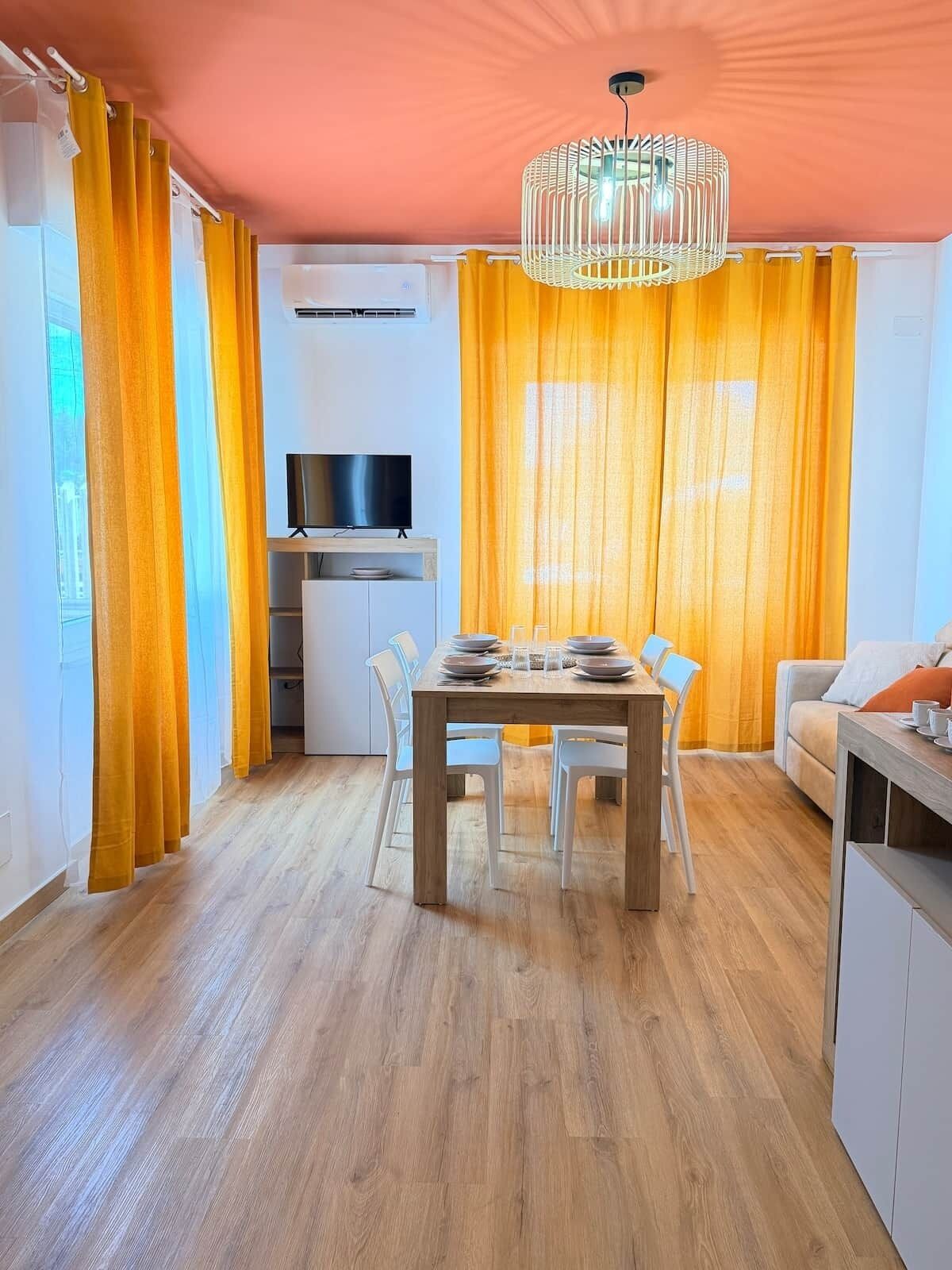 A dining area with a wooden table, white chairs, and a TV above it.