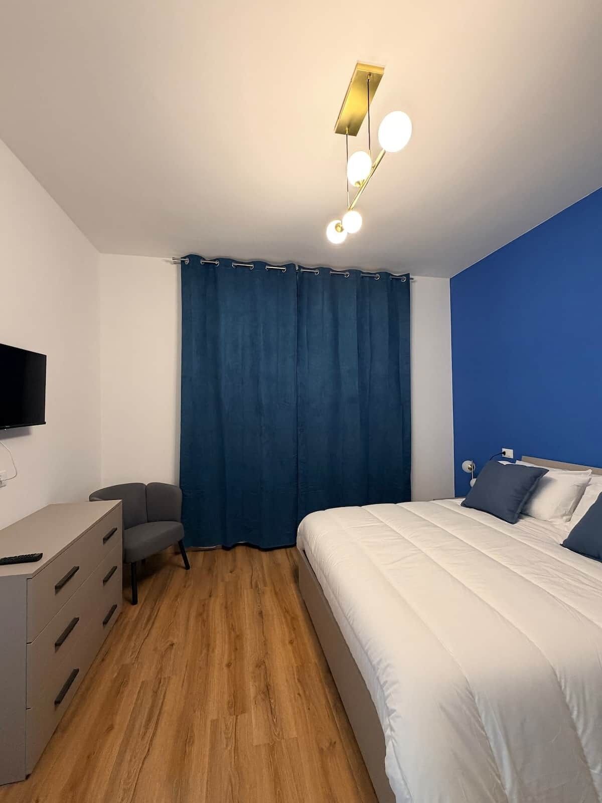 Una camera da letto moderna con un letto, una scrivania, una sedia, una televisione e una lampada a soffitto.
