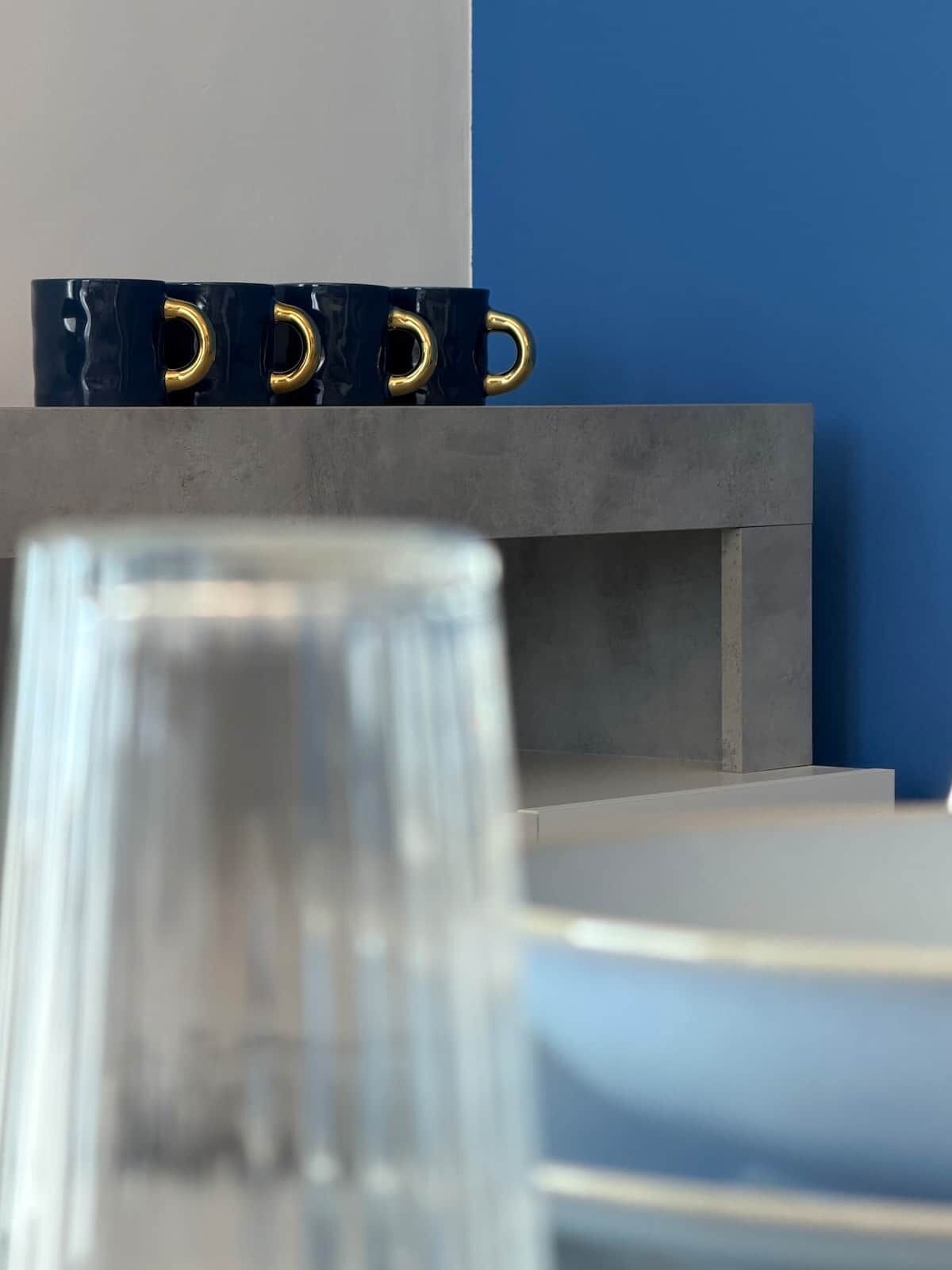 Ein Glastisch mit Metallgestell, eine blaue Wand und ein grauer Schrank.