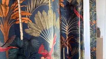 Une pièce décorée d’un rideau orné d’un motif de feuilles tropicales.