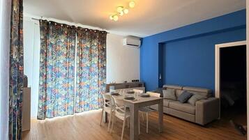 A modern living room with a dining area, blue accent wall, and a large window with curtains.