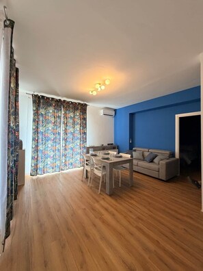 Un soggiorno moderno con zona pranzo, parete decorata in blu e un'ampia finestra con tende.