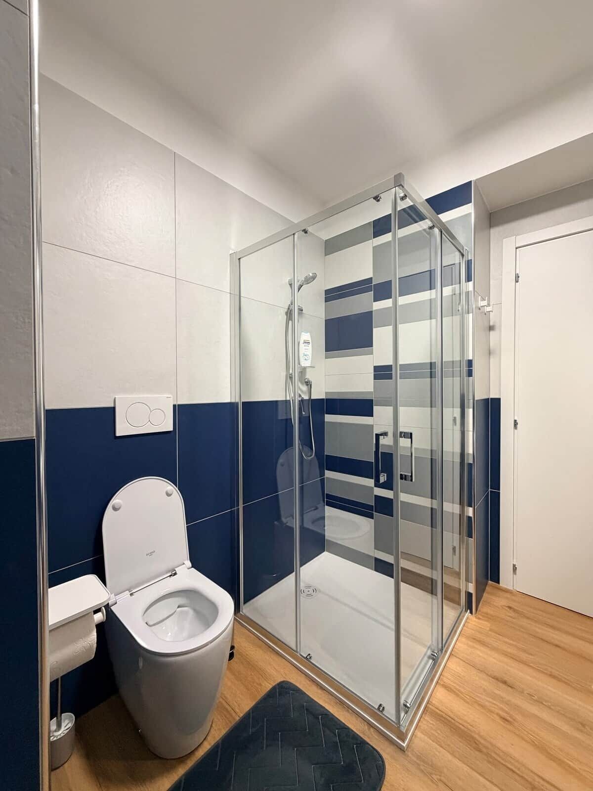 Ein modernes Badezimmer mit einer gläsernen Dusche, einer weißen Toilette und einer Wand mit blauen und weißen Fliesen.