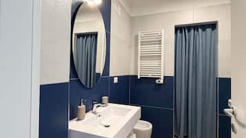 Un baño con lavamanos blanco, un espejo, toallero y cortina de ducha.