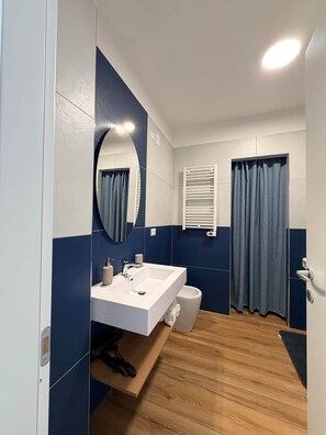 Un baño con lavamanos blanco, un espejo, toallero y cortina de ducha.