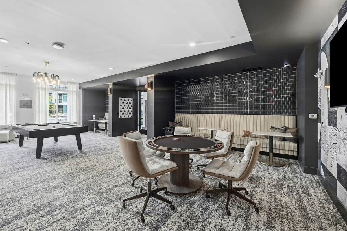 A modern lounge area with a pool table, a round table with chairs, and a seating area with a sofa and a TV.