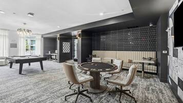 A modern lounge area with a pool table, a round table with chairs, and a seating area with a sofa and a TV.