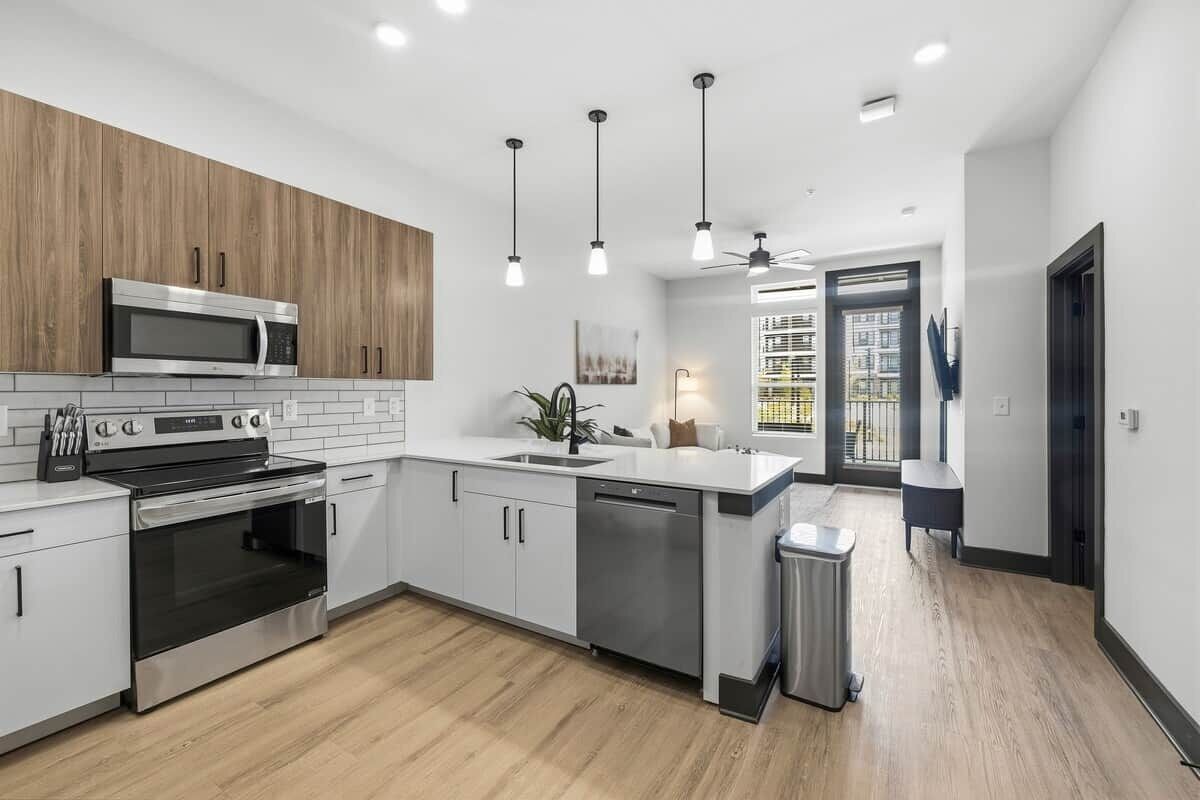 A modern kitchen with stainless steel appliances, a wooden accent wall, and pendant lighting.