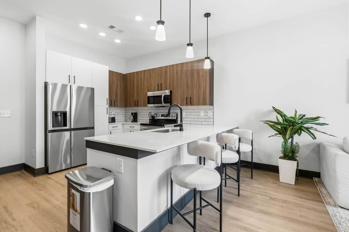 A modern kitchen with stainless steel appliances, a central island with bar stools, and a wooden accent wall.