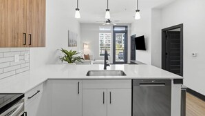 Een moderne keuken met een centraal eiland, hanglampen en uitzicht op de woonkamer.