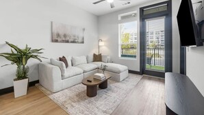 Een moderne woonkamer met een modulaire bank, een salontafel, een plafondventilator, een flatscreen-tv en een groot raam met jaloezieën.