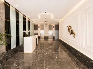 Eine moderne Hotelhalle mit Marmorboden, einer Rezeption und Aufzügen.